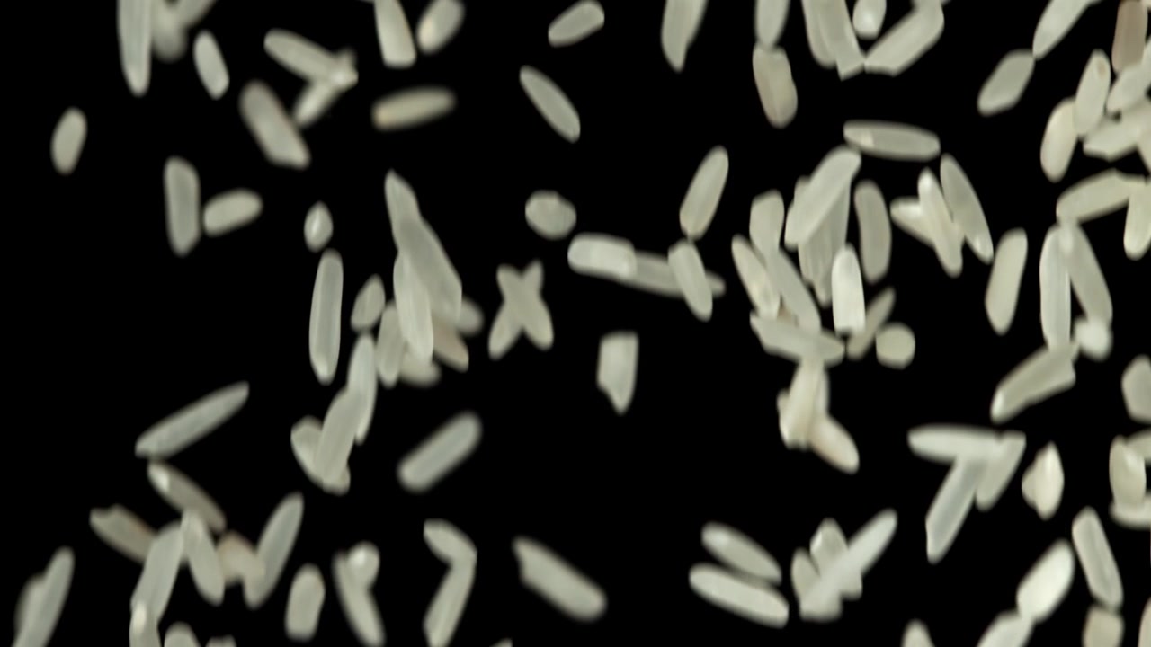 Ukogte hvide risgryn falder i slowmotion på sort baggrund