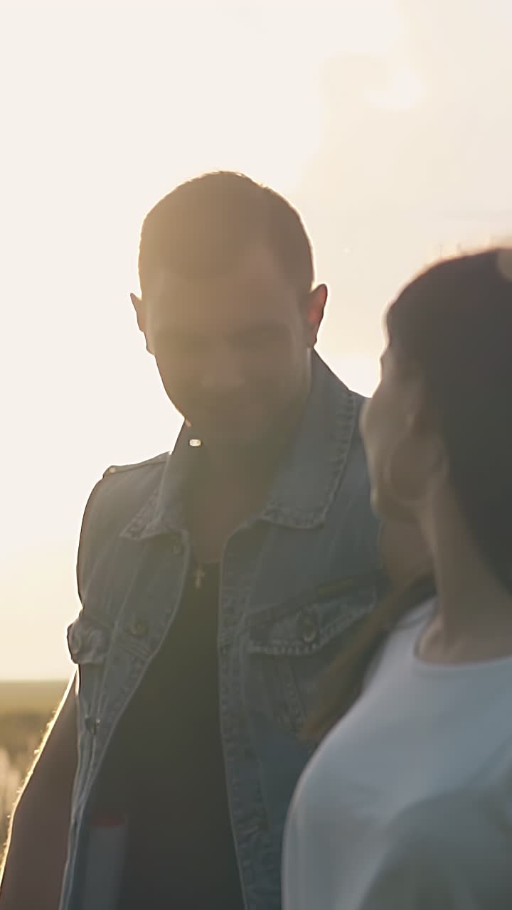 Close-up de linda garota morena com brincos correndo de mãos dadas com um homem bonito contra o sol brilhante do entardecer, em câmera lenta.