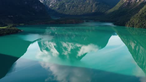 green pristine transparent lake between tall mountains in norway with reflection of the mountains