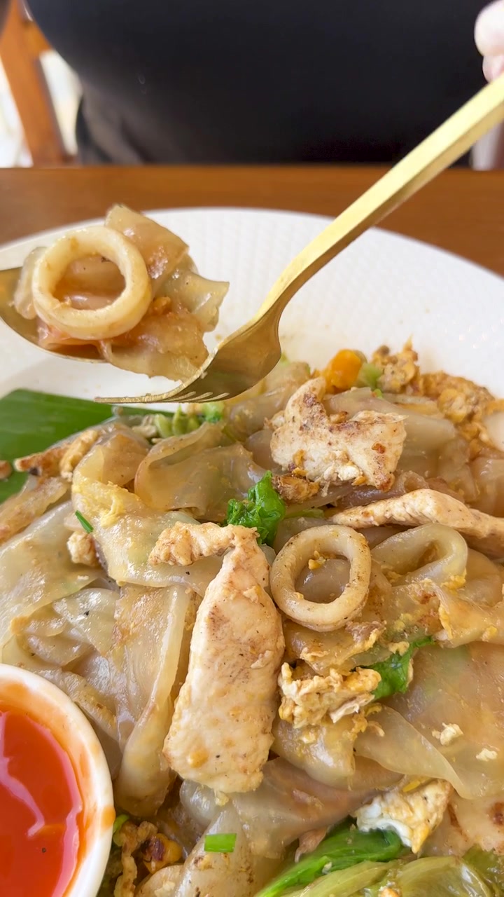 Toma cenital en primer plano de una persona usando un tenedor para comer fideos de arroz tailandeses salteados.
