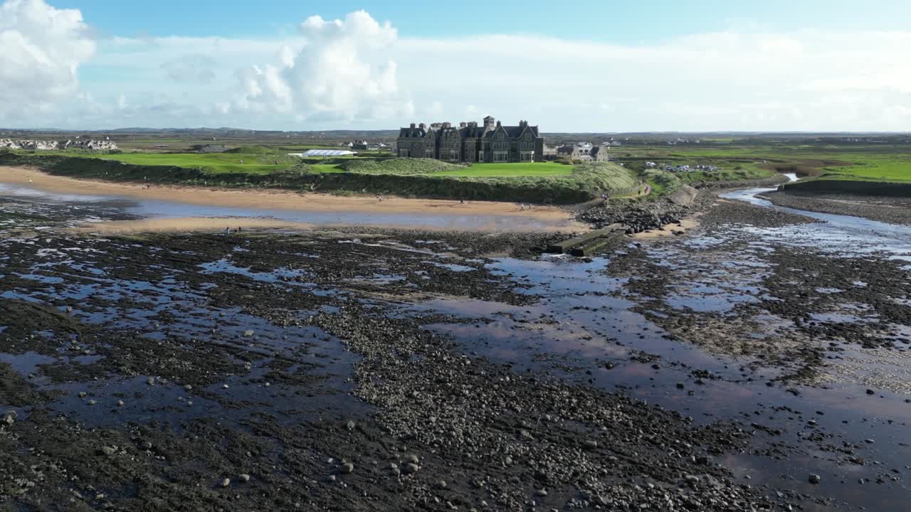 Low tide revealing rocky textures near a grand castle with lush fields in the background, at Dughmore bay