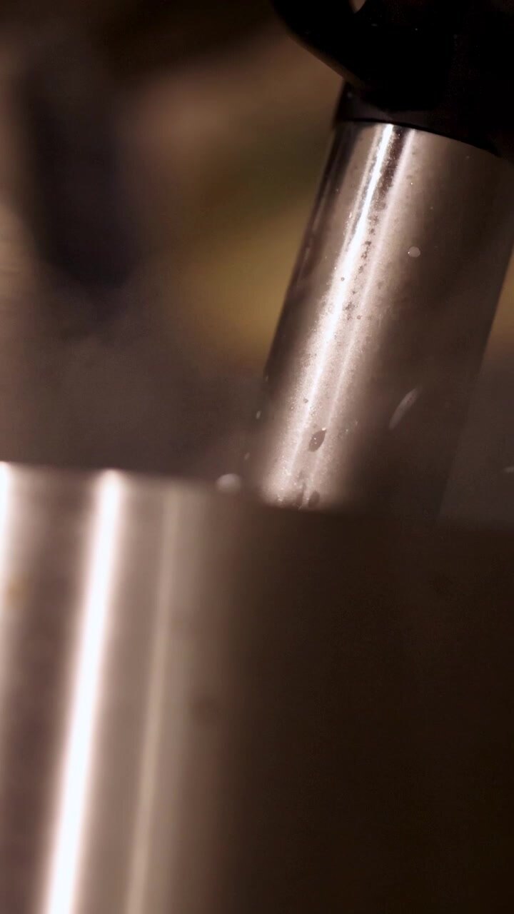 A detailed view of a milk frother steaming milk, highlighting the frothing action and steam in a warm kitchen setting