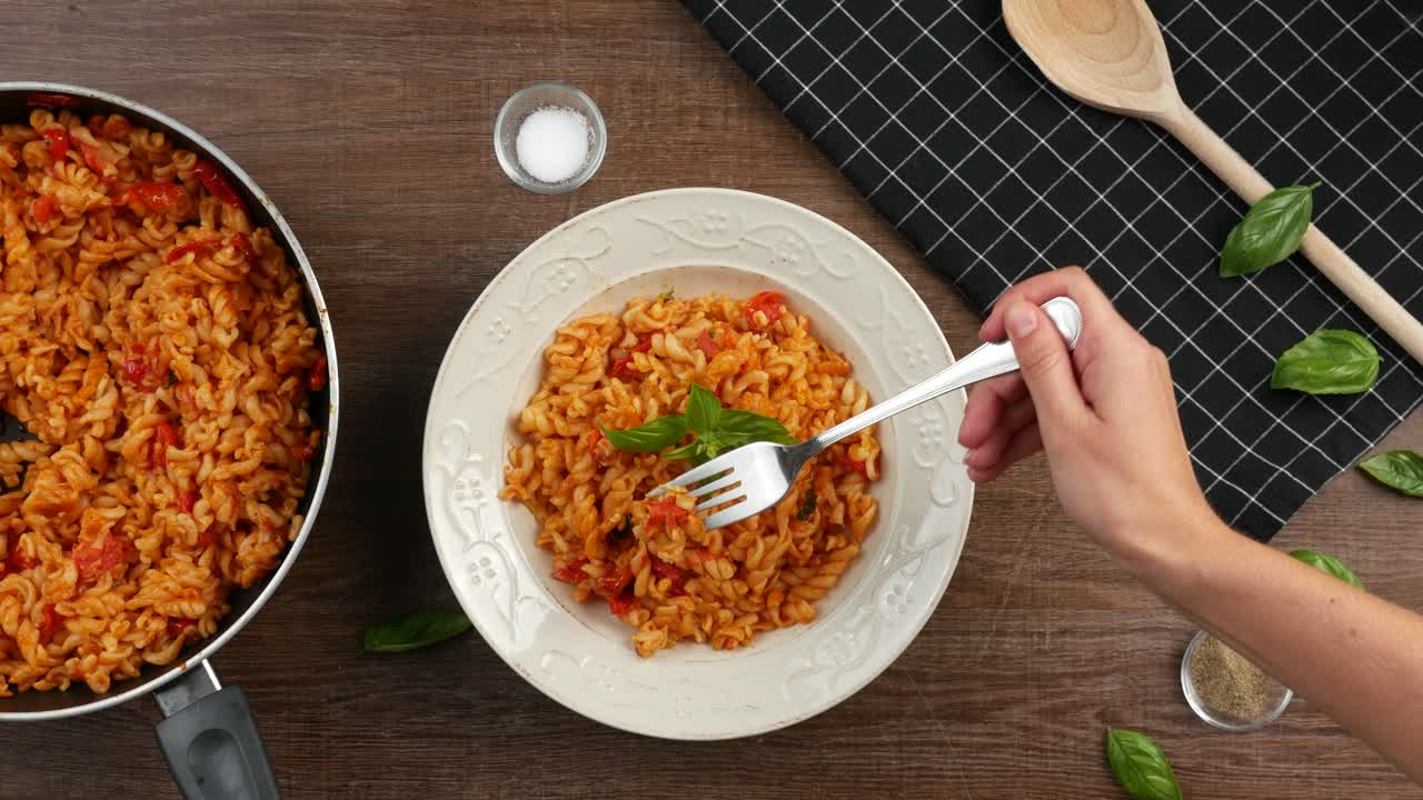 toma de arriba hacia abajo de adornar la pasta caprese italiana con hojas frescas de albahaca, luego clavar un tenedor en la pasta y levantarla con queso mozarella estirado