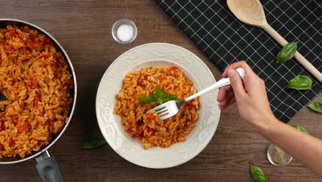 top down shot of garnishing italian caprese pasta with fresh basil leaves, then sticking fork into pasta and lifting it up with stretching mozarella cheese