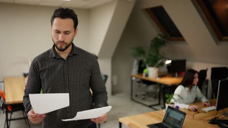 Office-worker-standing-at-modern-office-coworking-space-holding-pile-of-papers