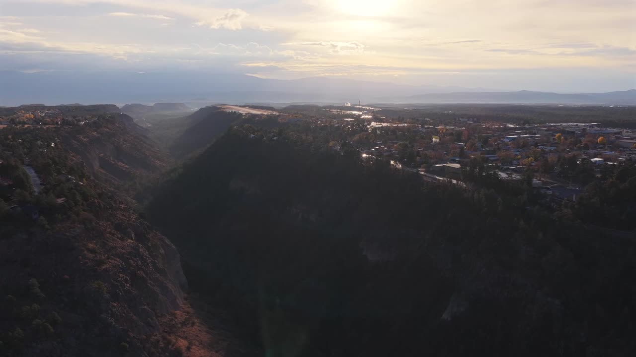 Wide aerial tracking shot continuing high over the expansive canyon gorge. Steep walls and dense high-desert forest are illuminated by atmospheric sunrise light