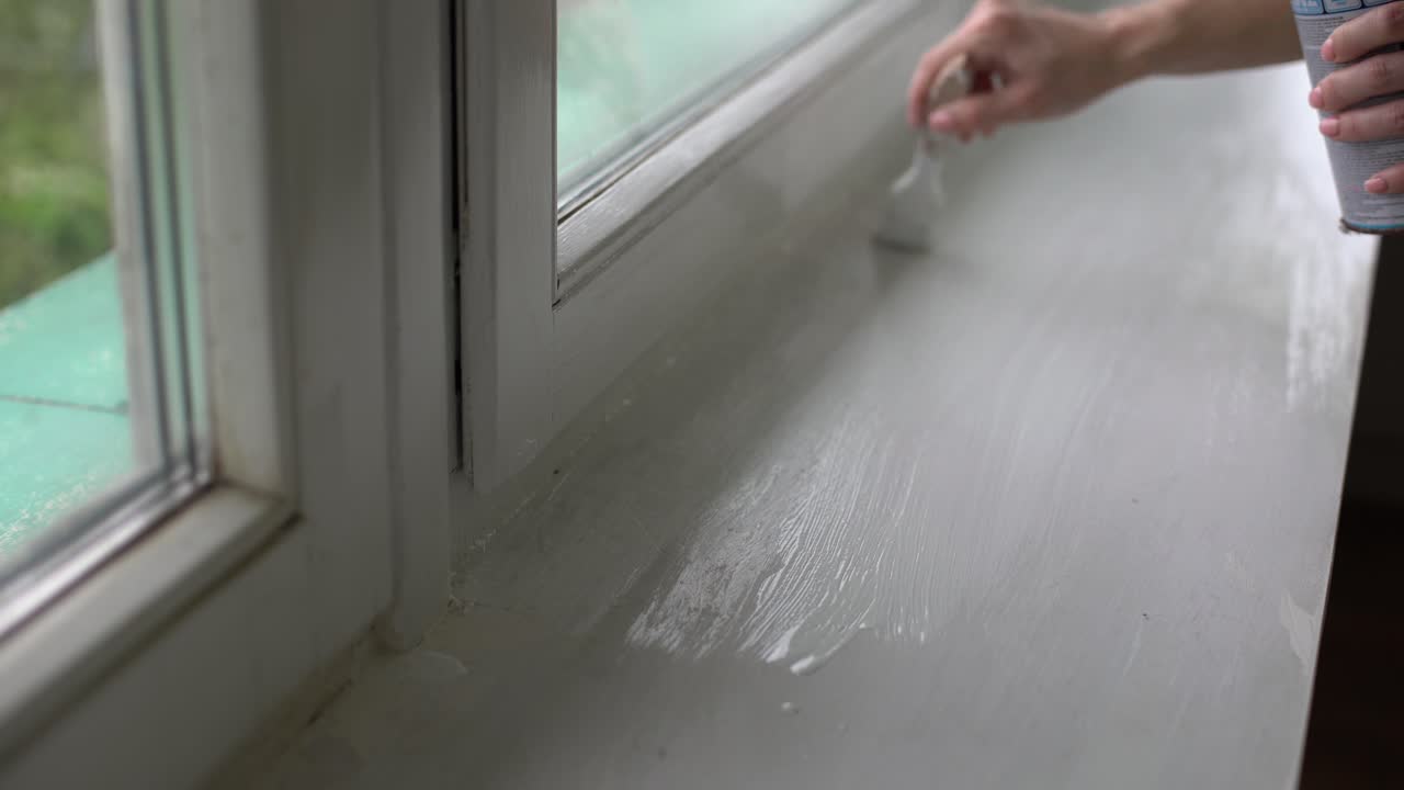 한 여자가 창문의 경사면을  ⁇ 색 페인트로 칠하고, 창문의 구 ⁇ 을  ⁇ 솔로 칠하고, 창문 프레임을  ⁇ 색 페인트의 롤러로 칠합니다.