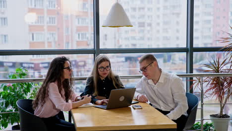 co-workers solving problems, discussing strategies in office. teammates sit at desk in front of laptop puzzled with some work issues, thinking over some moments.