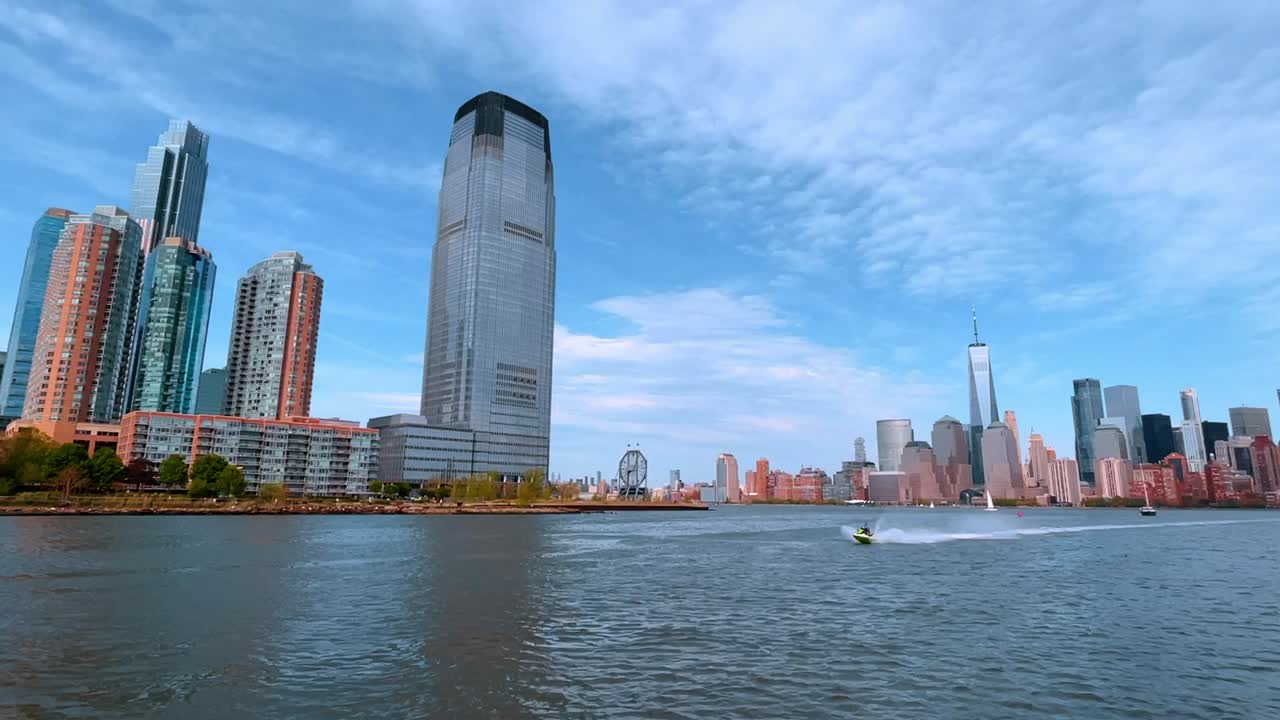 Vista panorâmica do horizonte de Manhattan a partir do Rio Hudson. Vista distante dos arranha-céus de Nova Iorque e do One World Trade Center do outro lado da água com nuvens leves.