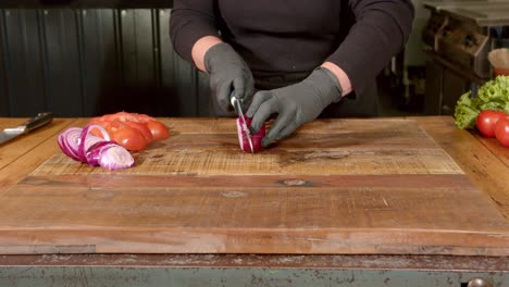 red onion being sliced on a wooden chopping board with plastic gloves on