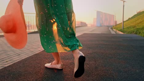 A Serene Sunset Stroll: A Woman in a Flowing Dress Enjoying a Beautiful Evening Walk by the Water&#039;s Edge with a Wide-brimmed Hat