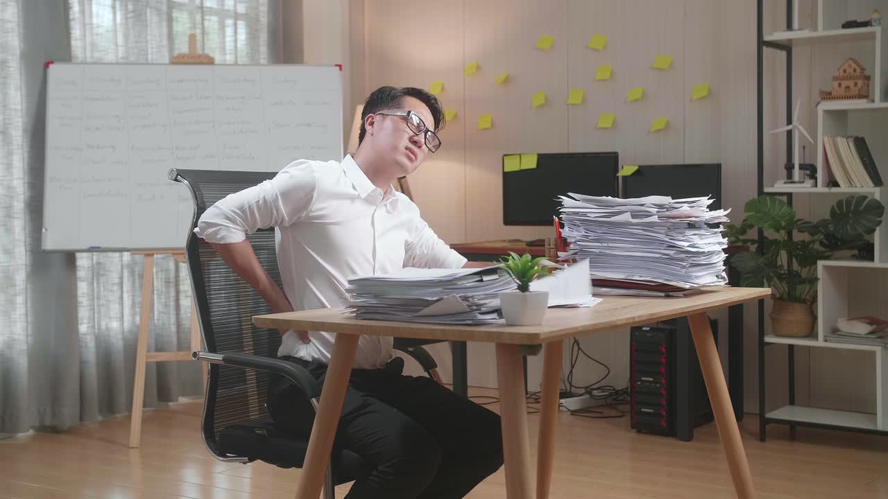 Asian Man Having Backache While Working Hard With Documents At The Office