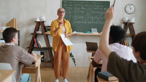 Female-Teacher-Explaining-Formulas-on-Chalkboard-to-Students