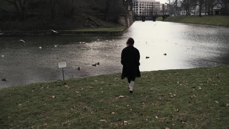 mujer joven con un abrigo negro caminando en un parque con un mar en otoño por la tarde