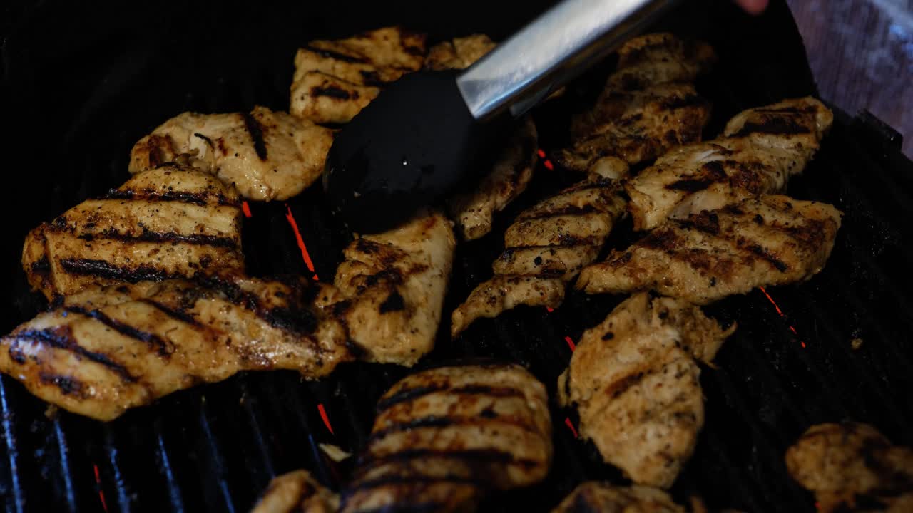 pollo asado a la parrilla eléctrica durante la barbacoa de verano, y volteado a mano con uñas pintadas de rojo y tong grabber