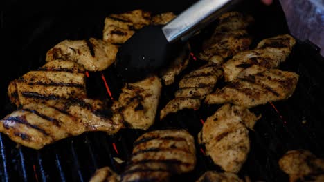 chicken being grilled on electric grill during summer barbecue, and being flipped by hand with red painted fingernails and tong grabber