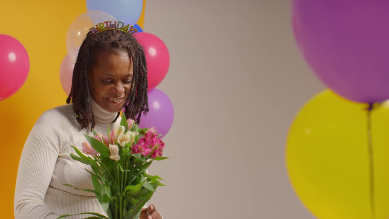retrato de estudio de una mujer con una cinta para la cabeza de cumpleaños sosteniendo un ramo de flores celebrando con globos 2
