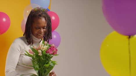 retrato de estudio de una mujer con una cinta para la cabeza de cumpleaños sosteniendo un ramo de flores celebrando con globos 2