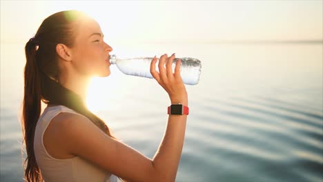 woman drinking water at sunrise by the lake