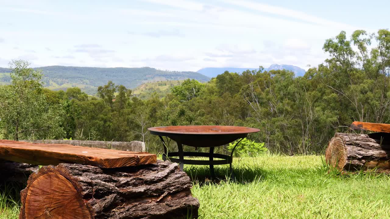 A serene view of wooden log benches facing expansive greenery and distant hills under a clear sky.