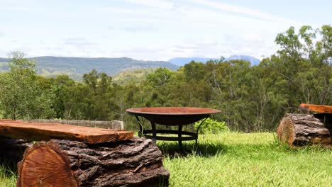 a serene view of wooden log benches facing expansive greenery and distant hills under a clear sky.