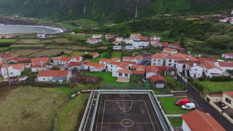 fly above soccer court at fajã grande town with waterfall in background