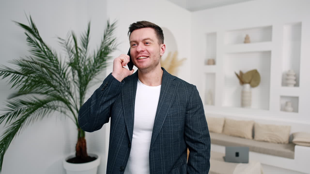 Positive easy-going man talking on the phone. Caucasian man in jacket communicating with clients from home.