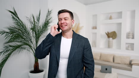 positive easy-going man talking on the phone. caucasian man in jacket communicating with clients from home.