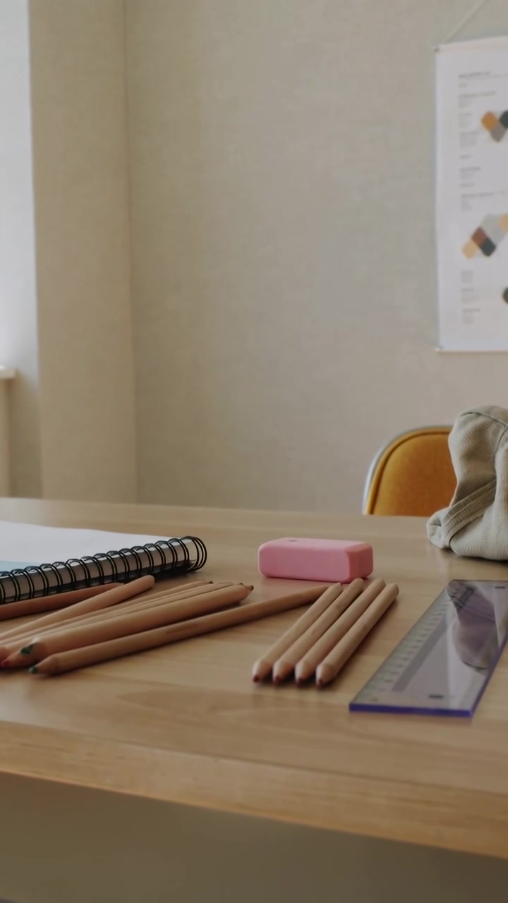 Vertical video: Panning camera revealing colored pencils, pink eraser and sketchbook at study desk