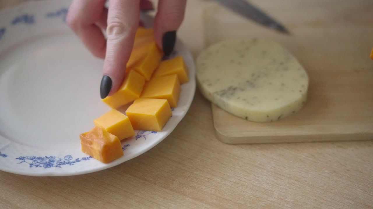 Disporre il cheddar su un piatto. Ragazza che prepara spuntini in cucina. Primo piano. Unghie nere