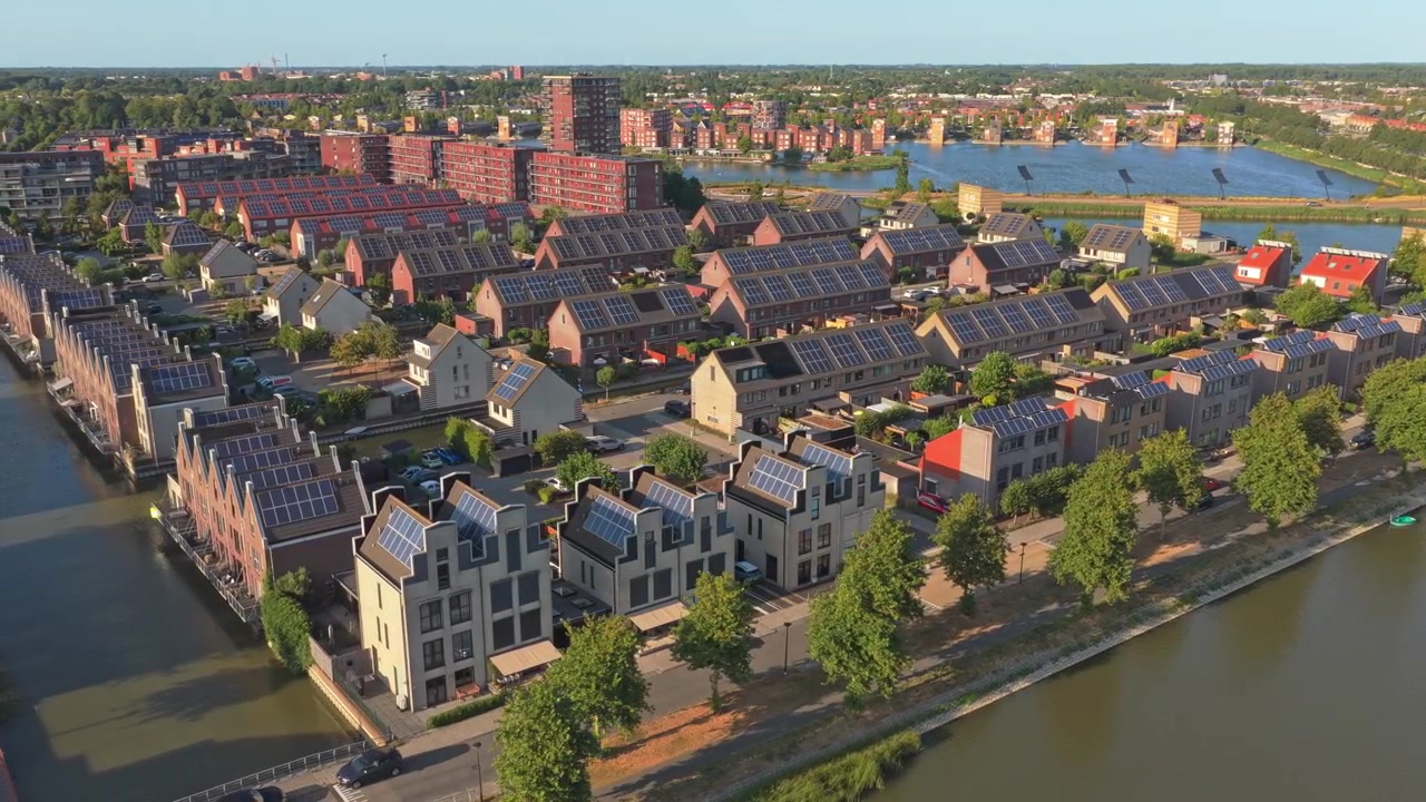 Prospettiva aerea soleggiata di un moderno quartiere olandese a Heerhugowaard, con case sul canale dotate di pannelli solari e design sostenibile