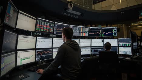 A glimpse into the bustling trading environment, showcasing focused individuals analyzing complex data on multiple screens in a modern financial trading room