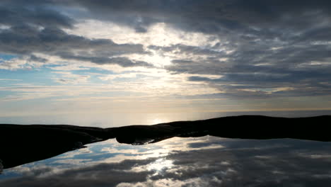 Atemberaubende-Bewegungszeitraffer-Einer-Sich-Bewegenden-Wolkenlandschaft-über-Klippen,-Die-Sich-Im-Endlosen-Ozean-Spiegeln