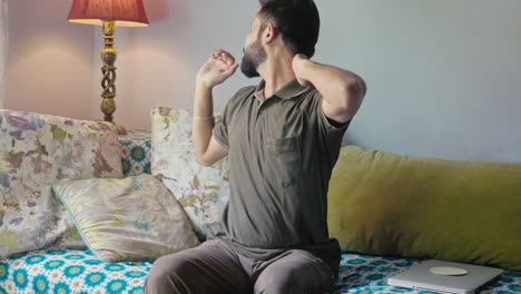 neck pain, health care. at home an indian man having neck pain while sitting on a sofa