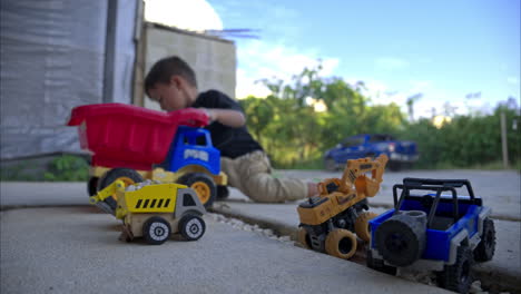 Young-mexican-boy-dumping-rocks-into-his-red-toy-dump-truck-sitting-on-the-sidewalk-in-the-afternoon