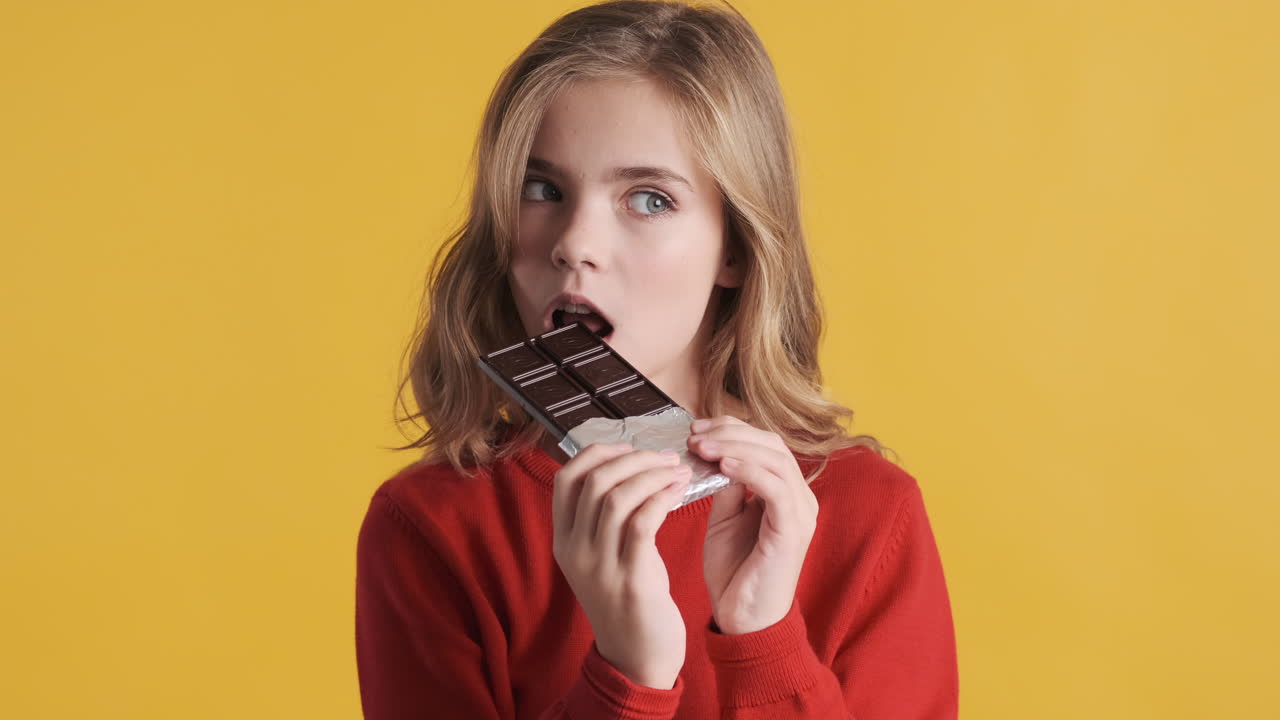 십대 백인 소녀가 카메라 앞에서 초콜릿 바를 먹고 있습니다.