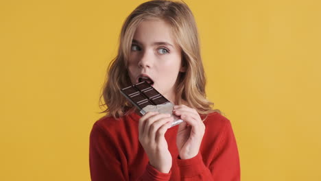 teenage caucasian girl eating chocolate bar in front of the camera.