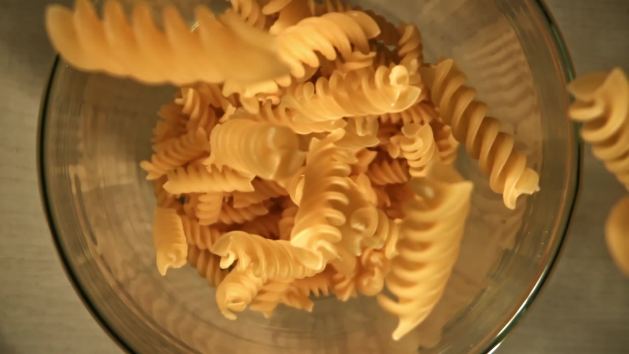 Movimento rallentato di fusilli che cadono in una ciotola di vetro