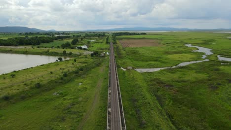 aerial reverse footage revealing an elevated railway through wetlands and farmlands, gorgeous landscape and lake, in saraburi, thailand