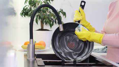 a woman washes a pan with a sponge and detergent work in the kitchen