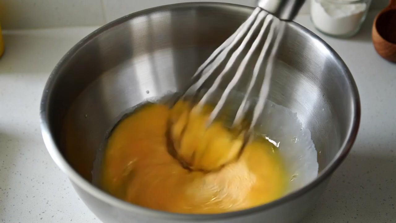 Metalen garde die eidooiers en eiwitten ronddraaiend mengt in een stalen kom op het aanrecht, met een pot.