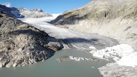 Luftaufnahme-Des-Rhonegletschers-In-Der-Nähe-Des-Furkapasses-An-Der-Grenze-Zwischen-Wallis-Und-Uri-In-Der-Schweiz-Mit-Einem-Schwenk-Vom-Eis-Zu-Den-Wasserfällen-Am-Ende-Des-Sees