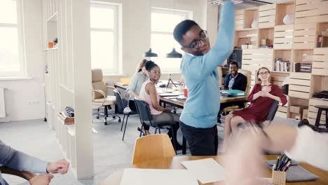 un feliz hombre afroamericano da los cinco a sus colegas de oficina, celebrando el éxito comercial con un baile alegre en 4k.