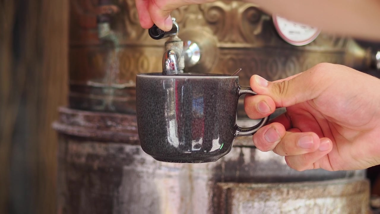 Person Filling a Mug with Hot Water from a Vintage Samovar