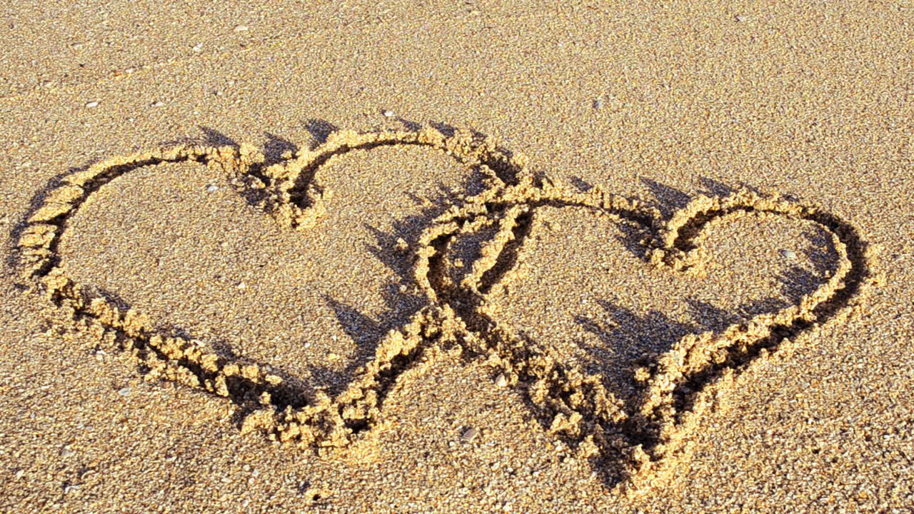 Un cuore disegnato sulla sabbia. Il cuore viene cancellato da un'onda marina. Riprese sulla spiaggia.