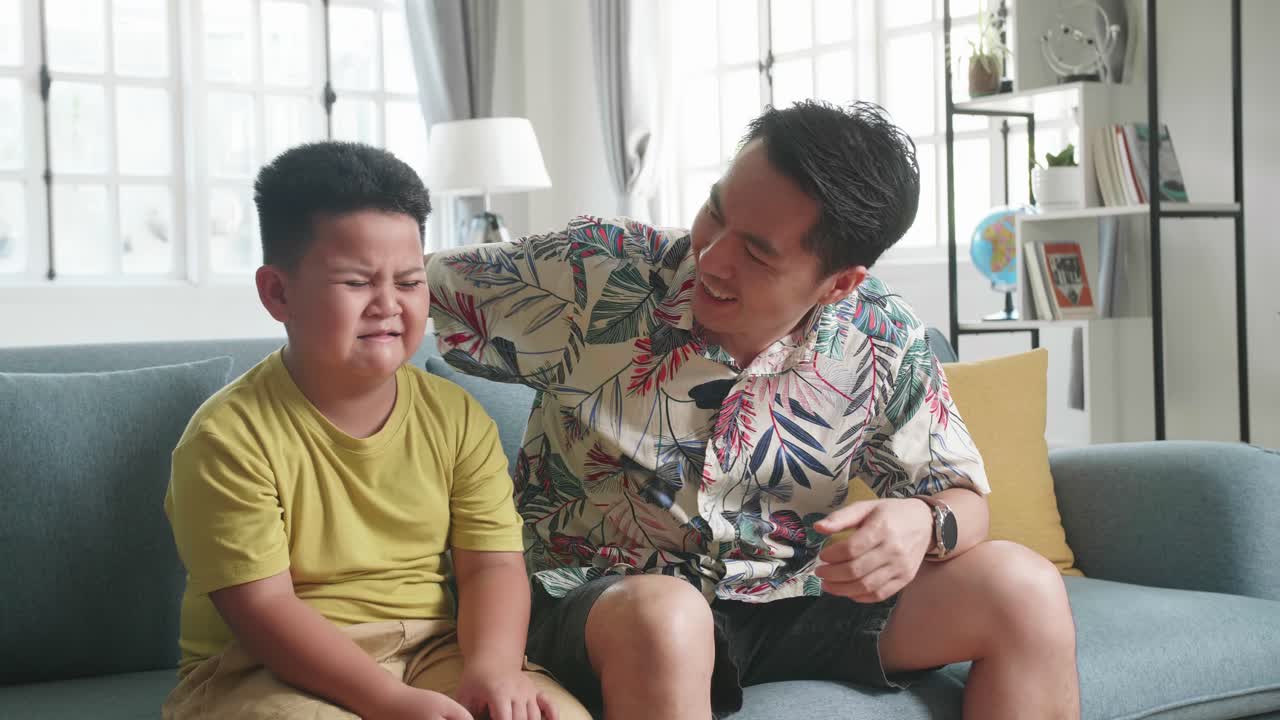 Child Cry While Sitting With His Father On A Couch And Watching Tv