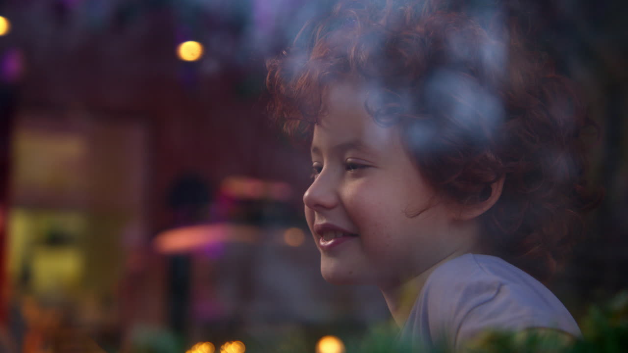 Child with red curly hair looking out a window