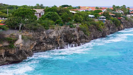 Caribbean-ocean-waves-crash-and-spray-mist-backwash-against-tall-sea-cliffs-in-Curacao,-aerial