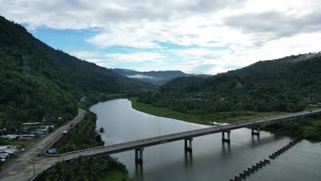establecimiento de una vista aérea del puente moderno sobre el río tropical con un impresionante paisaje nuboso y exuberantes montañas en el fondo