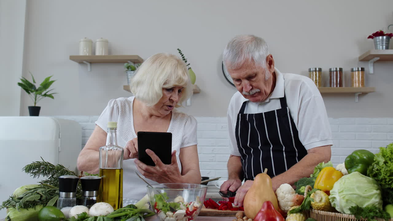 abuelos veganos mayores que buscan una receta culinaria en línea en una tableta digital, cocinando ensalada
